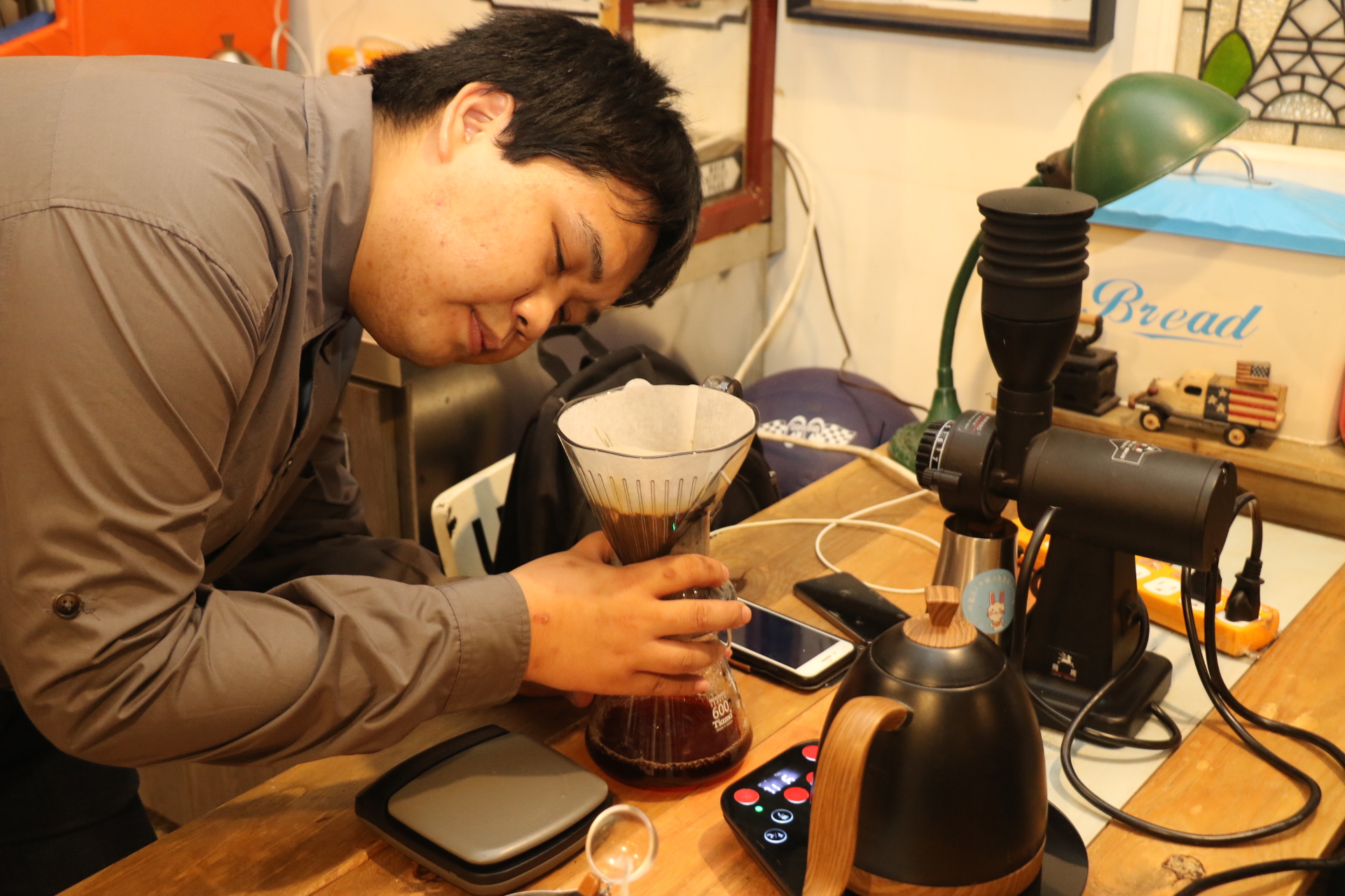 晉 宏 學 習 沖 泡 咖 啡 仰 賴 兩 支 手 機 與 藍 芽 溫 控 壺 和 語 音 磅 秤 等 輔 具 。 